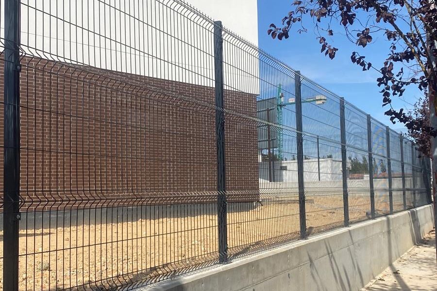 Vallado de panel plegado gris sobre muro de hormigón junto a un edificio